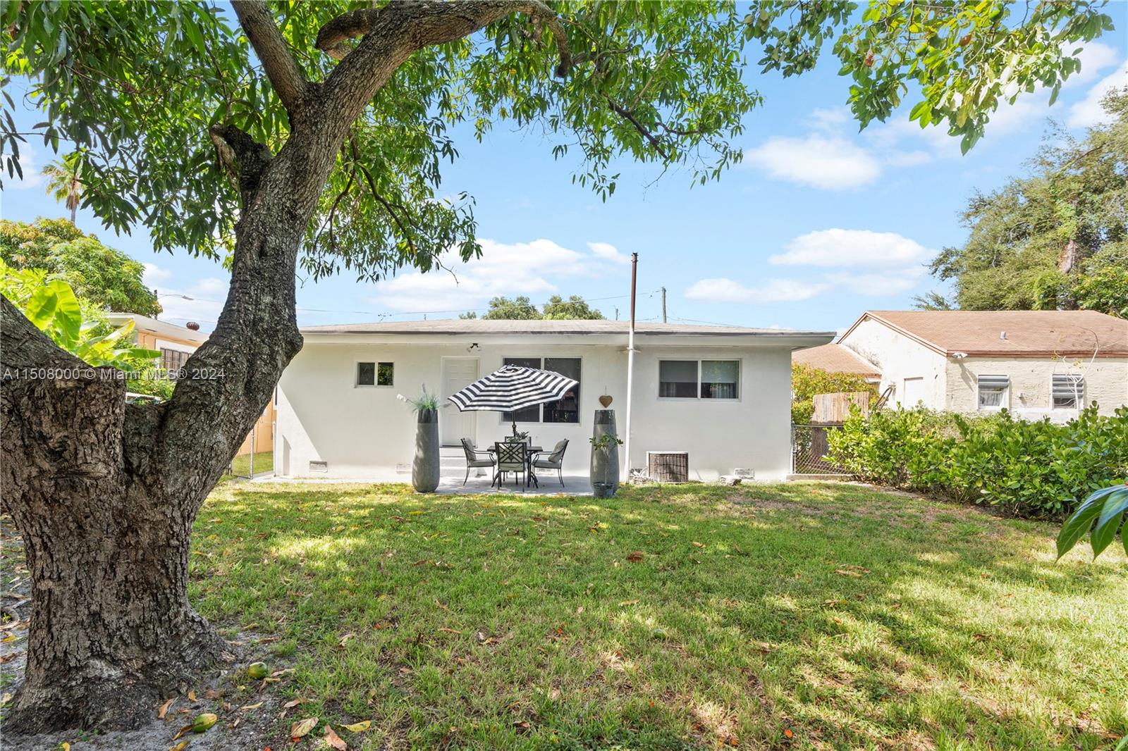 The backyard features a white house with a patio, outdoor dining set, and large tree — 236 NW 42nd St, Miami FL 33127, MIAMI, FL