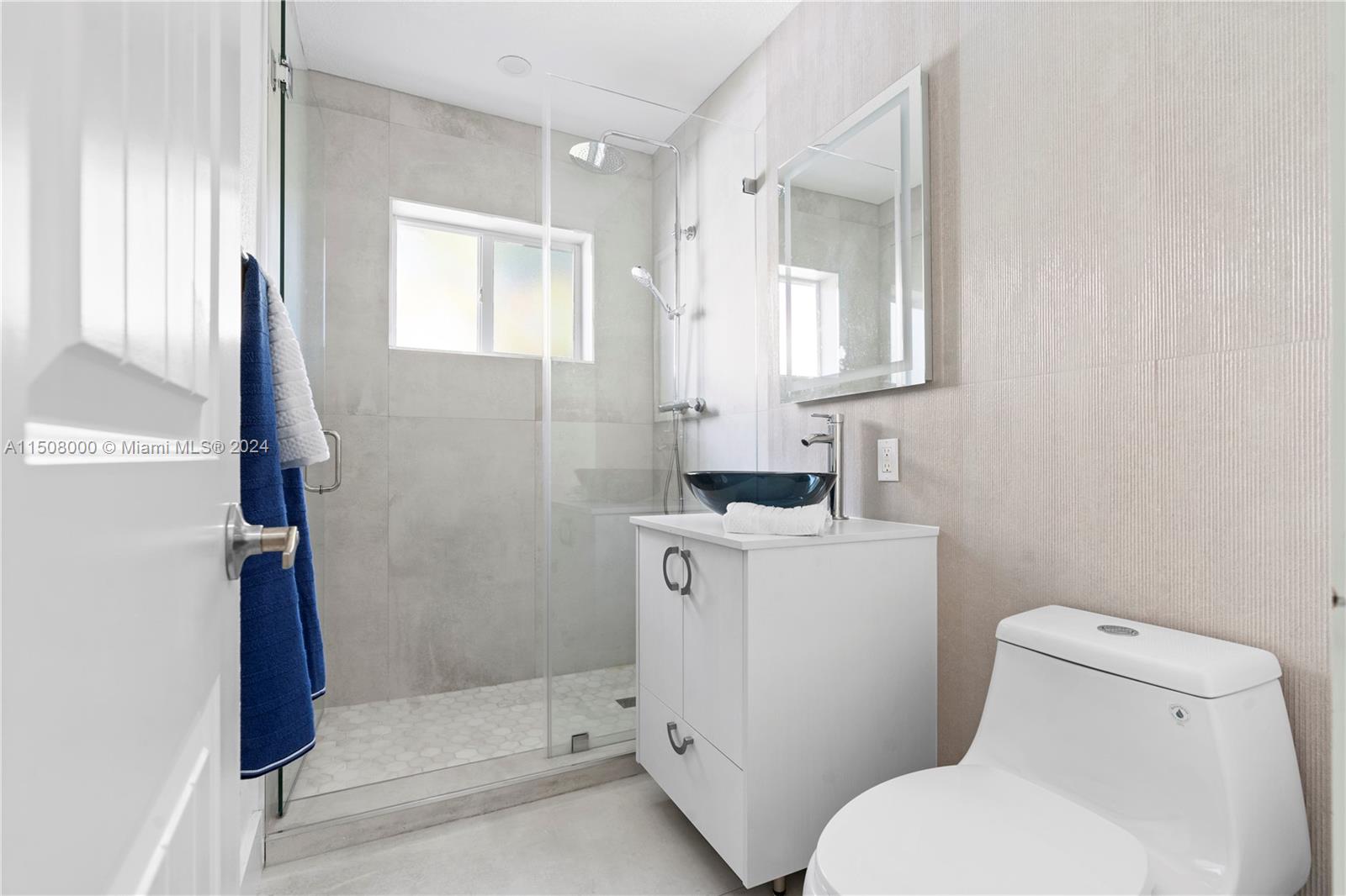 A modern bathroom features a glass-enclosed shower, a white vanity with a blue vessel sink, and a toilet — 236 NW 42nd St, Miami FL 33127, MIAMI, FL