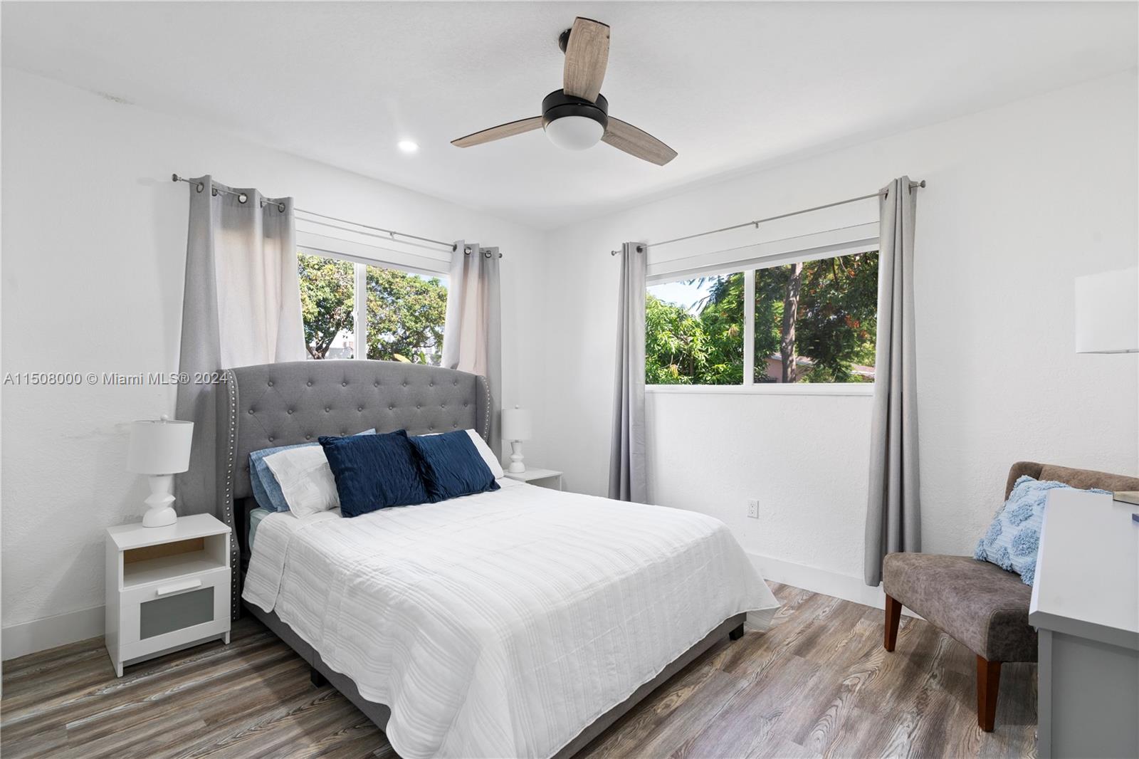 A bedroom features a gray tufted headboard, wood-look flooring, a ceiling fan, and two windows — 236 NW 42nd St, Miami FL 33127, MIAMI, FL