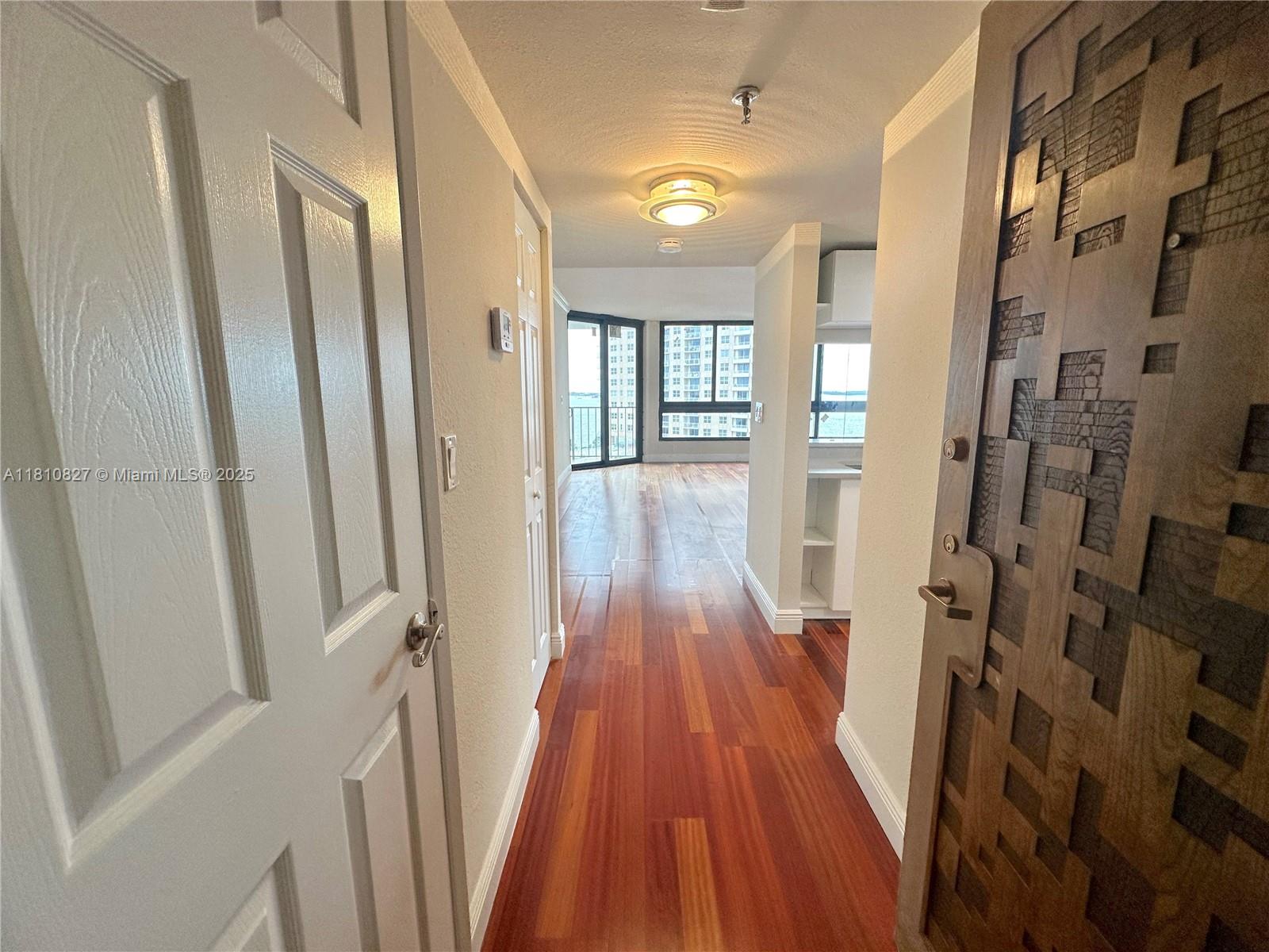 A hallway with hardwood floors leads toward a living area with large windows and views — 520 Brickell Key Dr # A811, Miami FL 33131, MIAMI, FL