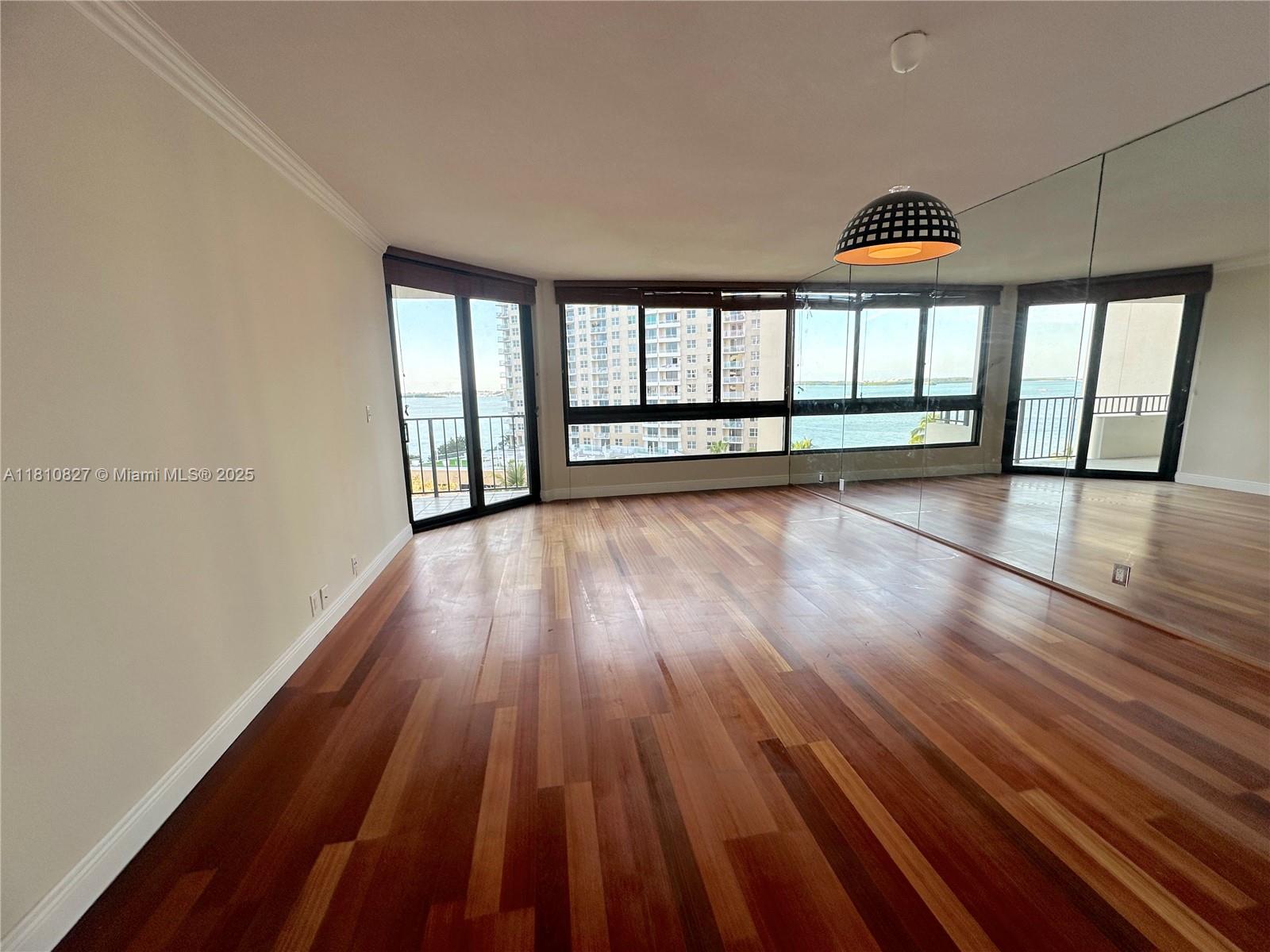 An empty room features hardwood floors, a mirrored wall, and large windows overlooking the water — 520 Brickell Key Dr # A811, Miami FL 33131, MIAMI, FL