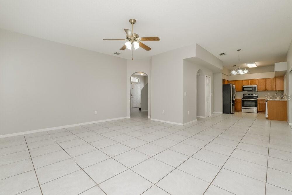An open-concept living area with light-colored tile flooring and a kitchen in the background — 13516 PRESTWICK DRIVE, RIVERVIEW, FL