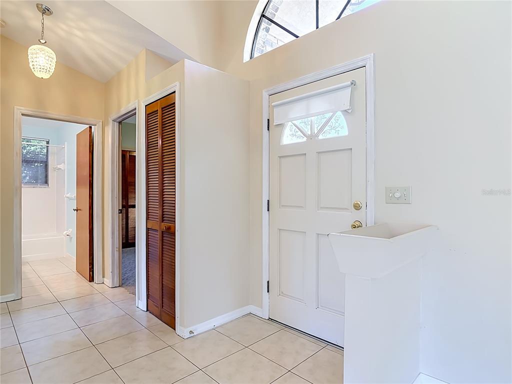 An entryway features a white door, tiled floors, a louvered closet, and a pedestal sink — 209 MEADOW LAKE DRIVE, EDGEWATER, FL