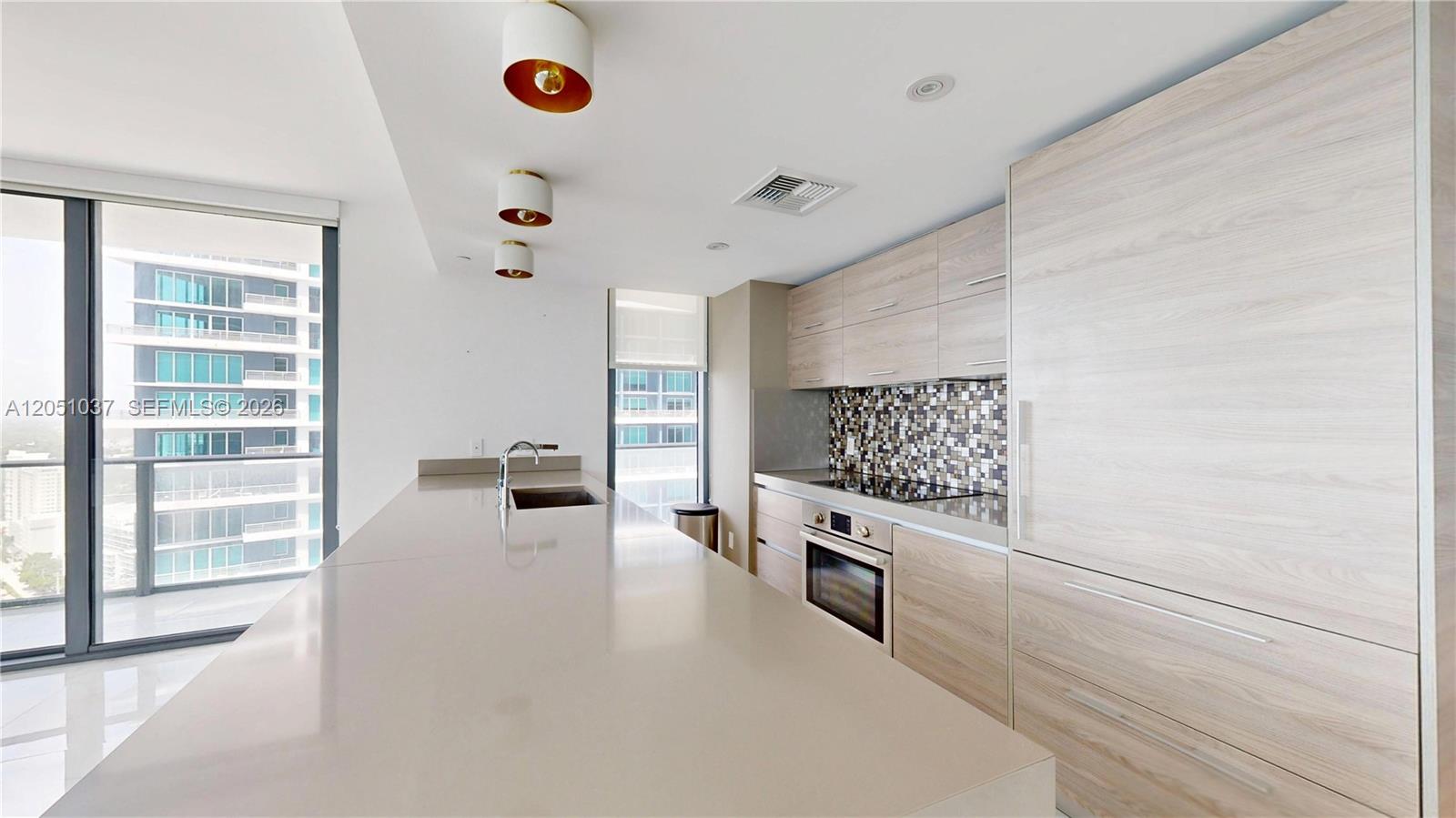 A modern kitchen features light wood cabinetry, a long quartz island, and a mosaic backsplash — 1300 S Miami Ave # 3106, Miami FL 33130, MIAMI, FL