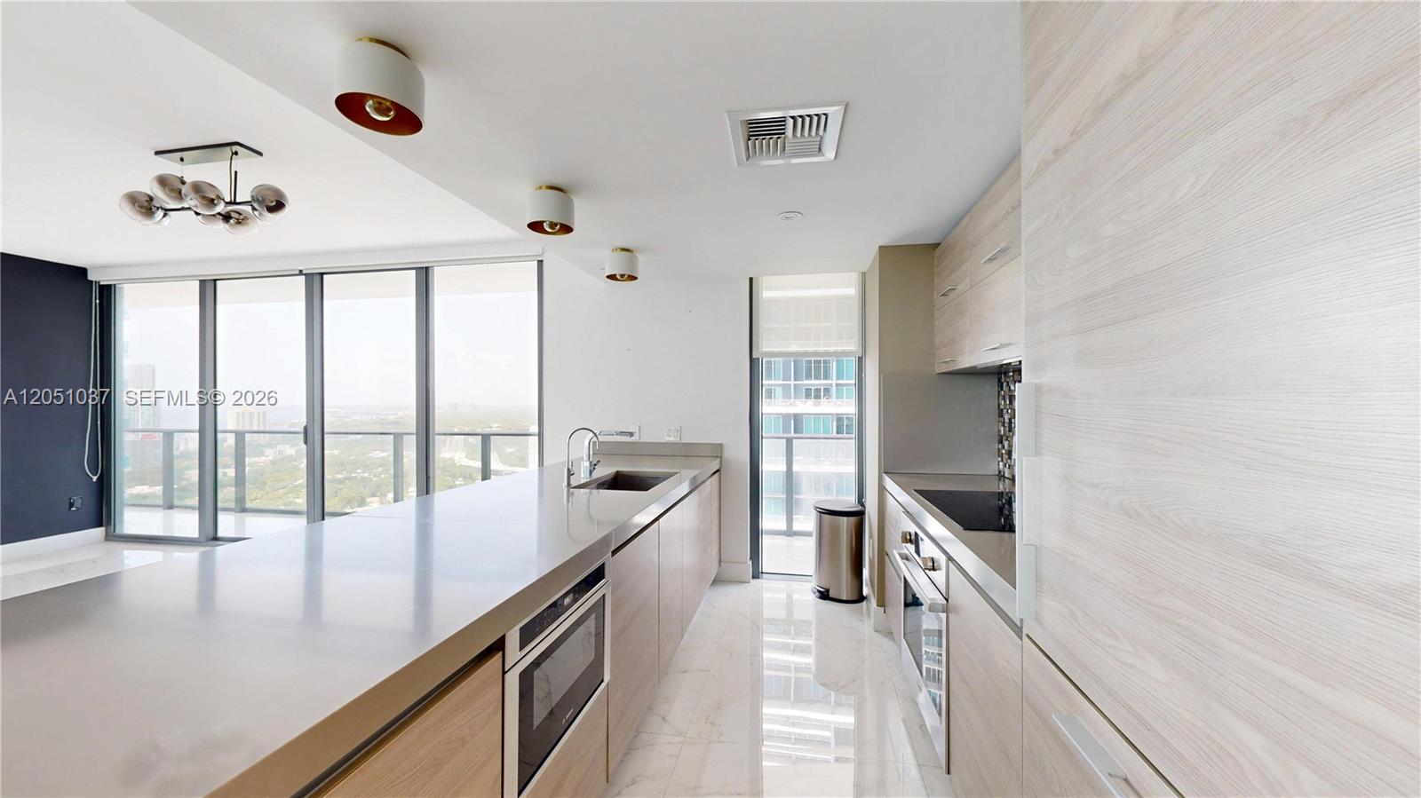 A modern kitchen features light wood cabinetry, stone countertops, and floor-to-ceiling windows with city views — 1300 S Miami Ave # 3106, Miami FL 33130, MIAMI, FL