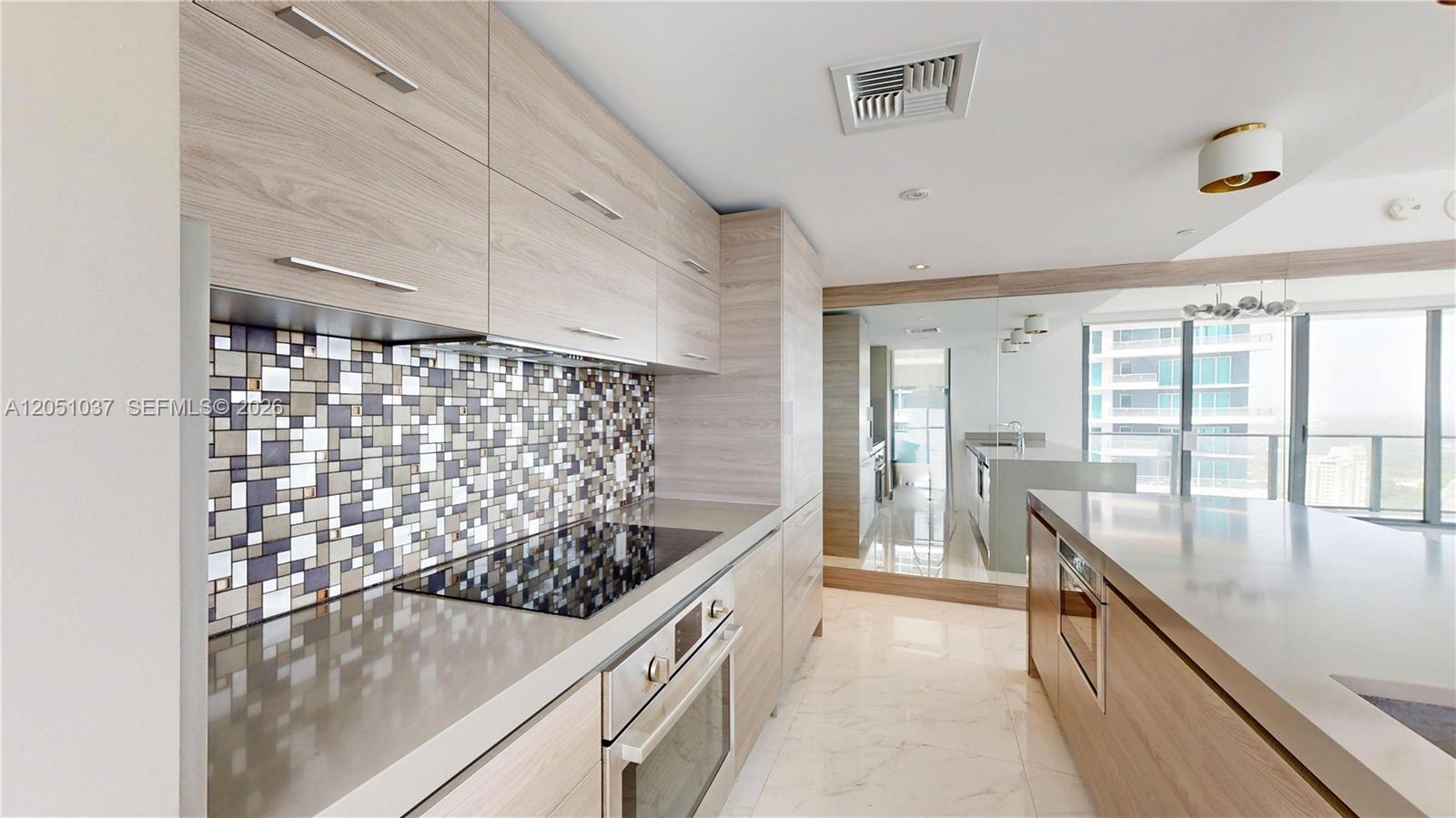 A modern kitchen features light wood cabinetry, a mosaic tile backsplash, and stainless steel appliances — 1300 S Miami Ave # 3106, Miami FL 33130, MIAMI, FL