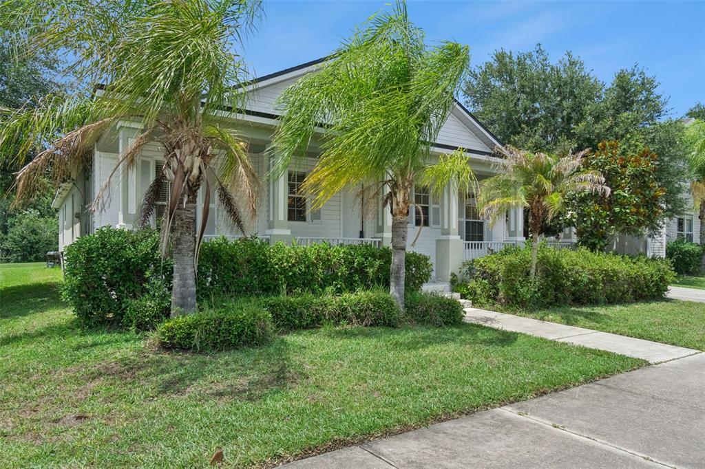 A white house with a front porch and palm trees sits behind a green hedge — 4957 PALL MALL STREET E, KISSIMMEE, FL