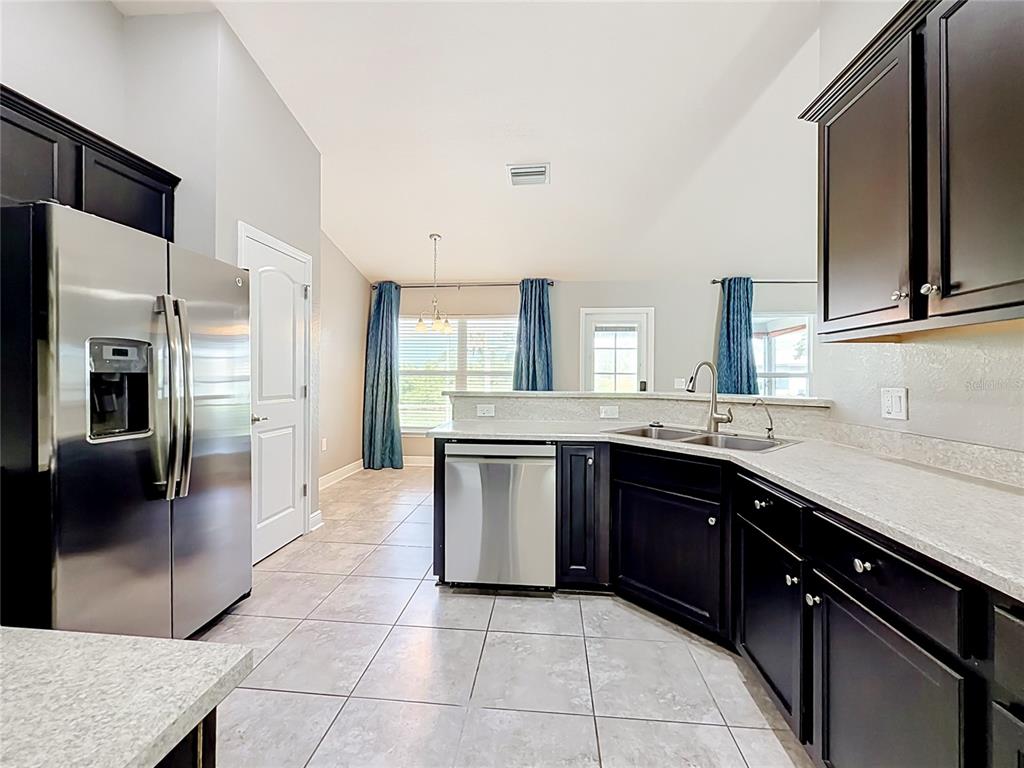 A kitchen with dark cabinets, stainless steel appliances, and light countertops overlooks a dining area — 1741 SHEVLIN STREET, NORTH PORT, FL