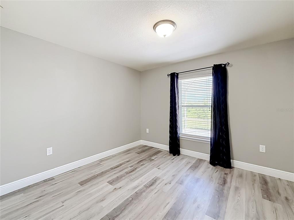 An empty bedroom features light gray walls, wood-look flooring, and a window with dark curtains — 1741 SHEVLIN STREET, NORTH PORT, FL