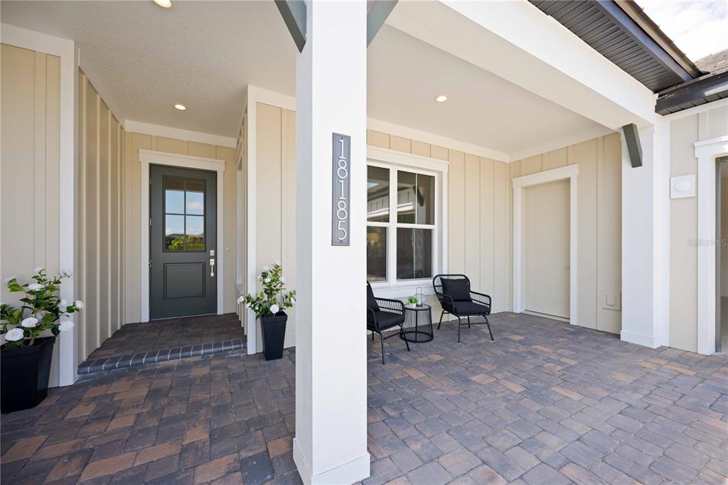 A covered front porch features a dark door, two black chairs, and a paved floor — 18185 HOME RUN DRIVE, VENICE, FL