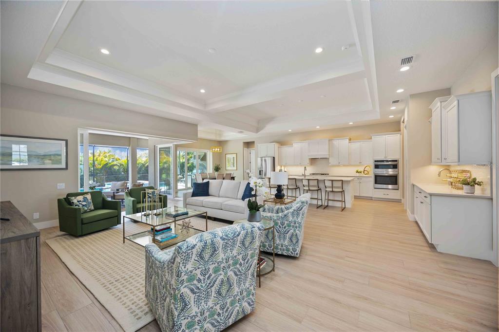 An open-concept living room and kitchen featuring white cabinetry, light wood flooring, and tray ceilings — 18185 HOME RUN DRIVE, VENICE, FL