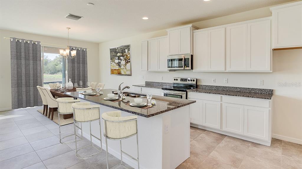 A kitchen with white cabinets, granite countertops, and an island with three bar stools — 17473 MAPLE GROVE ROAD, LAND O LAKES, FL