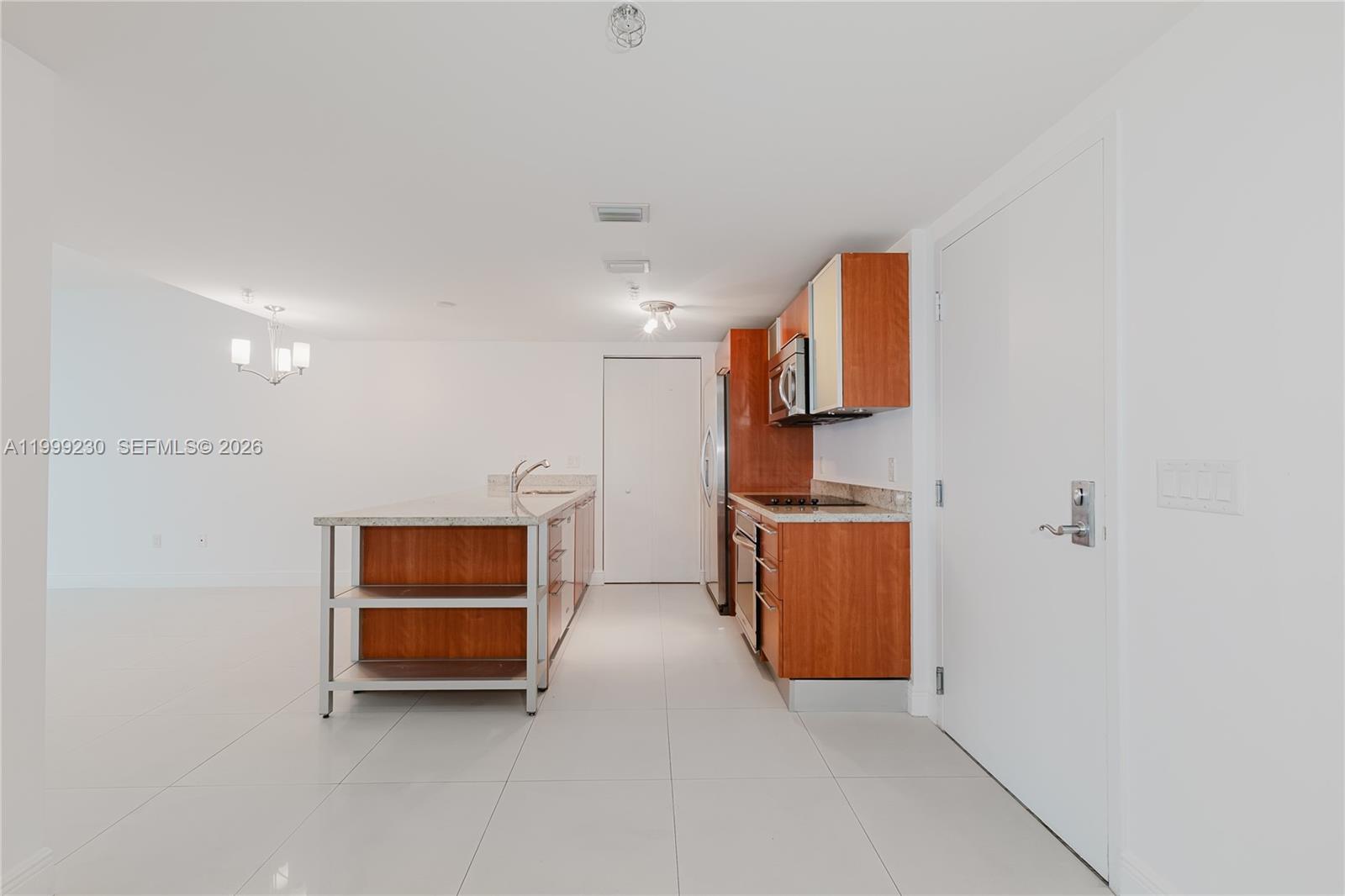 A modern kitchen features wood cabinets, granite countertops, a central island, and white tile flooring — 185 SW 7th St # 2007, Miami FL 33130, MIAMI, FL