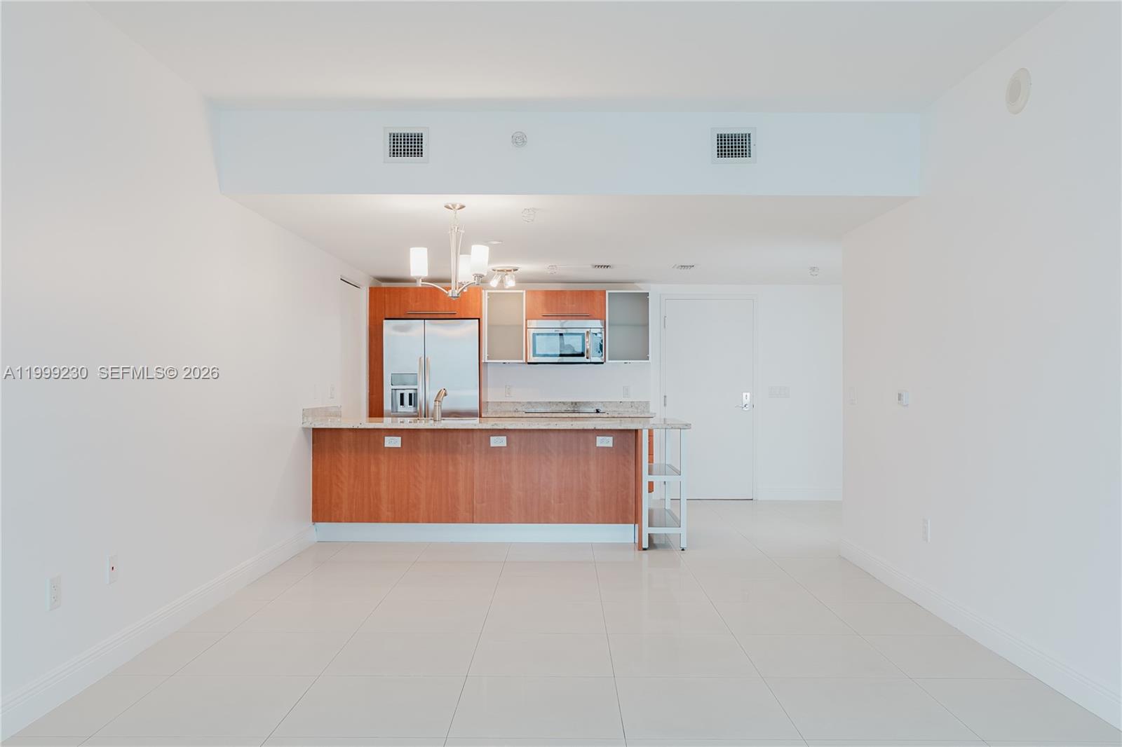 A kitchen with wood cabinets and granite countertops overlooks an open-concept living area — 185 SW 7th St # 2007, Miami FL 33130, MIAMI, FL