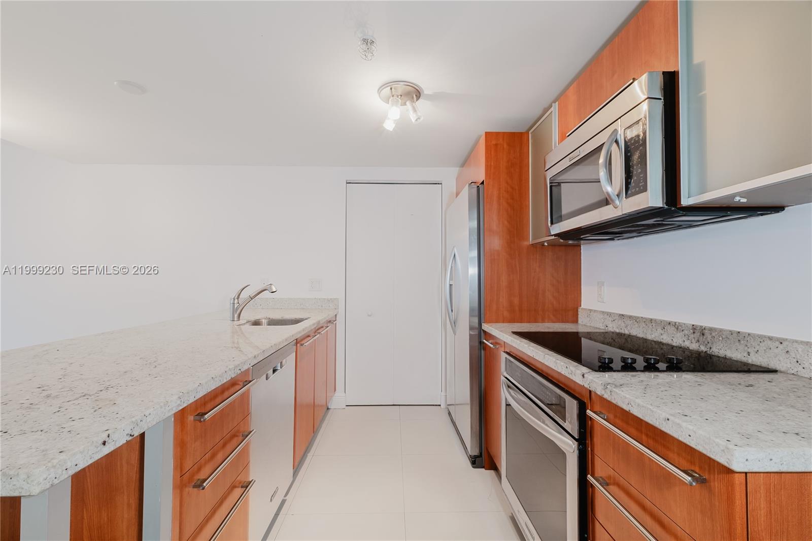 A galley kitchen features wood cabinets, granite countertops, and stainless steel appliances — 185 SW 7th St # 2007, Miami FL 33130, MIAMI, FL