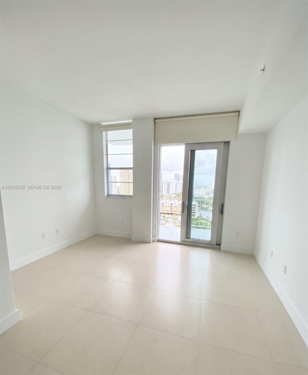 An empty room features white walls, light-colored tile flooring, a window, and a glass balcony door — 2829 Indian Creek Dr # 1405, Miami Beach FL 33140, MIAMI BEACH, FL
