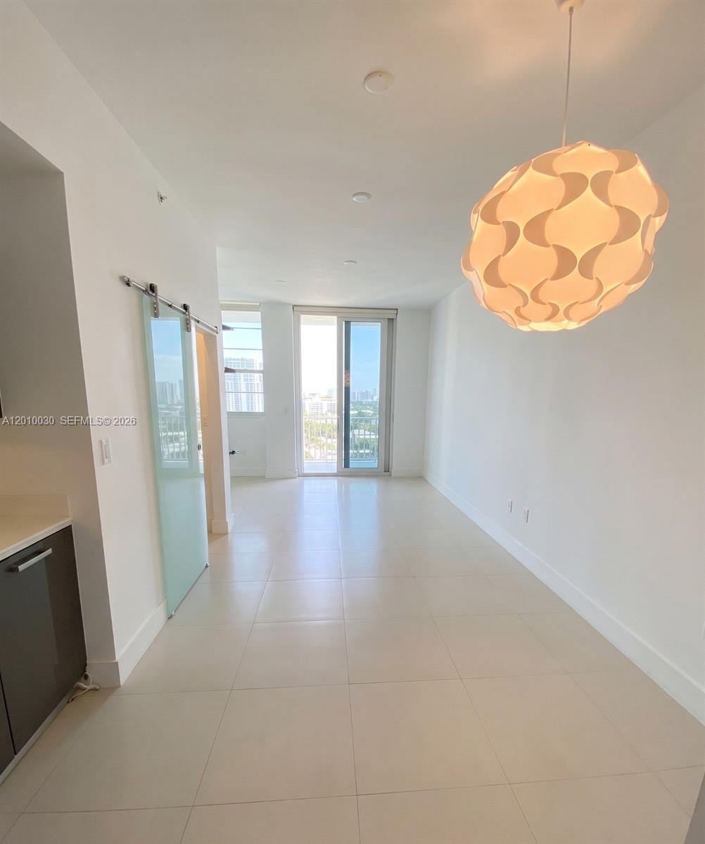 A bright, minimalist room features white walls, tile flooring, a modern pendant light, and sliding doors — 2829 Indian Creek Dr # 1405, Miami Beach FL 33140, MIAMI BEACH, FL