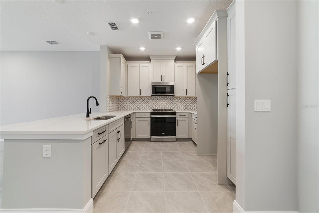 A modern kitchen features light gray cabinets, white countertops, stainless steel appliances, and tile flooring — 7557 LAUREATE BOULEVARD UNIT 6401, ORLANDO, FL