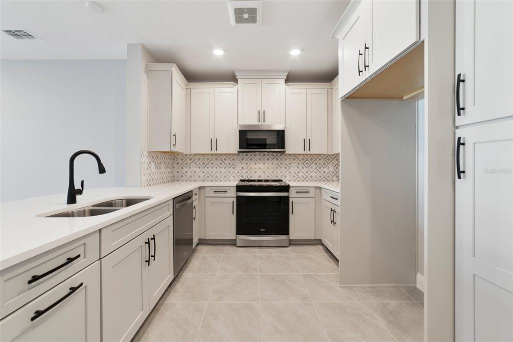 A modern kitchen features white cabinets, stainless steel appliances, a patterned backsplash, and quartz countertops — 7557 LAUREATE BOULEVARD UNIT 6401, ORLANDO, FL