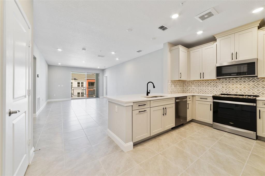A kitchen with light-colored cabinets, stainless steel appliances, and tile flooring opens to a living area — 7557 LAUREATE BOULEVARD UNIT 6401, ORLANDO, FL