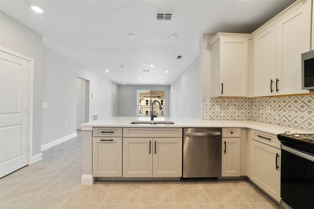 A kitchen with light-colored cabinets, stainless steel appliances, and a view of a balcony — 7557 LAUREATE BOULEVARD UNIT 6401, ORLANDO, FL