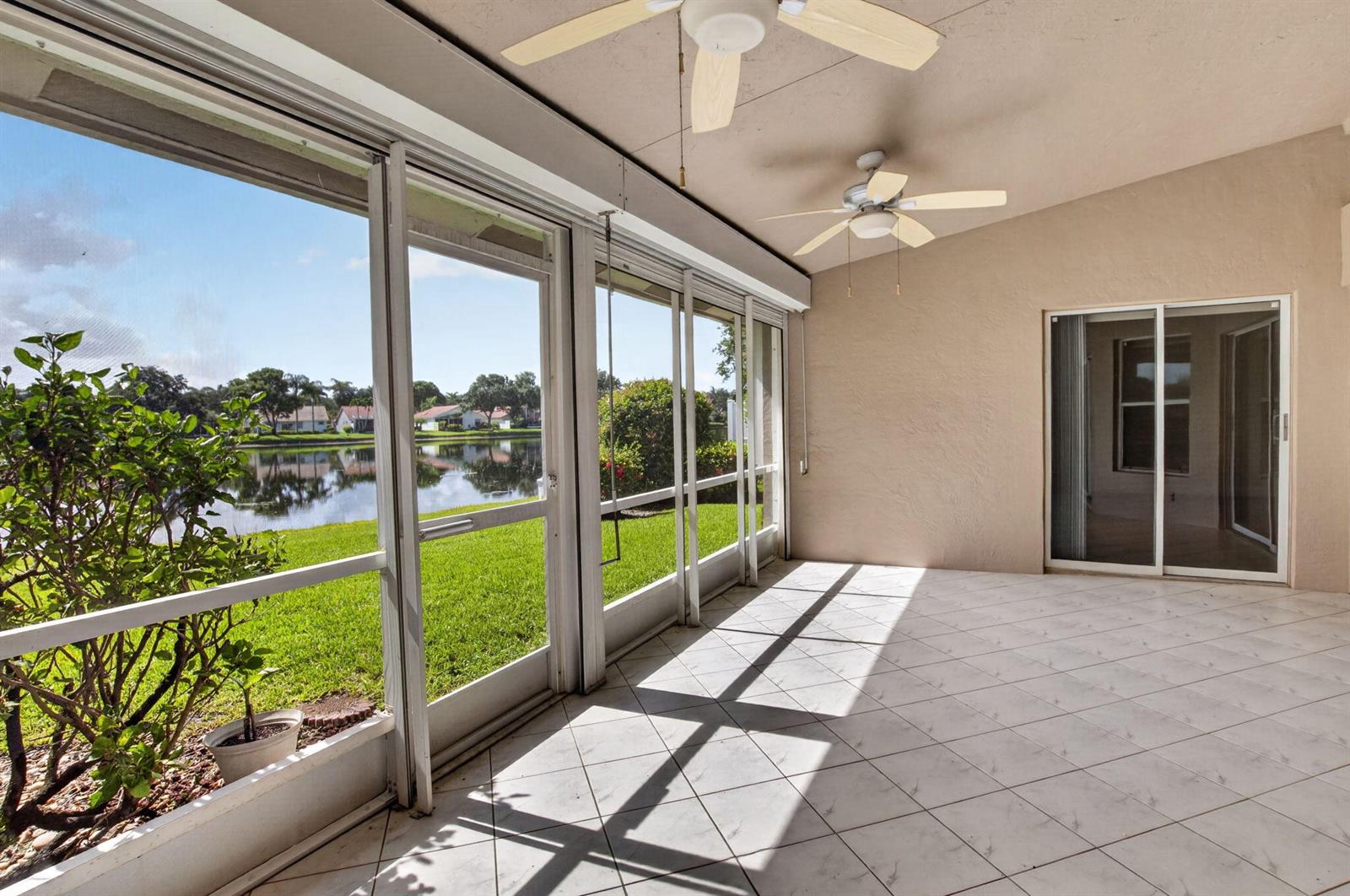 A tiled, screened-in patio overlooks a lake with a view of houses in the distance — 9875 Harbour Lake Circle, Boynton Beach FL 33437, BOYNTON BEACH, FL