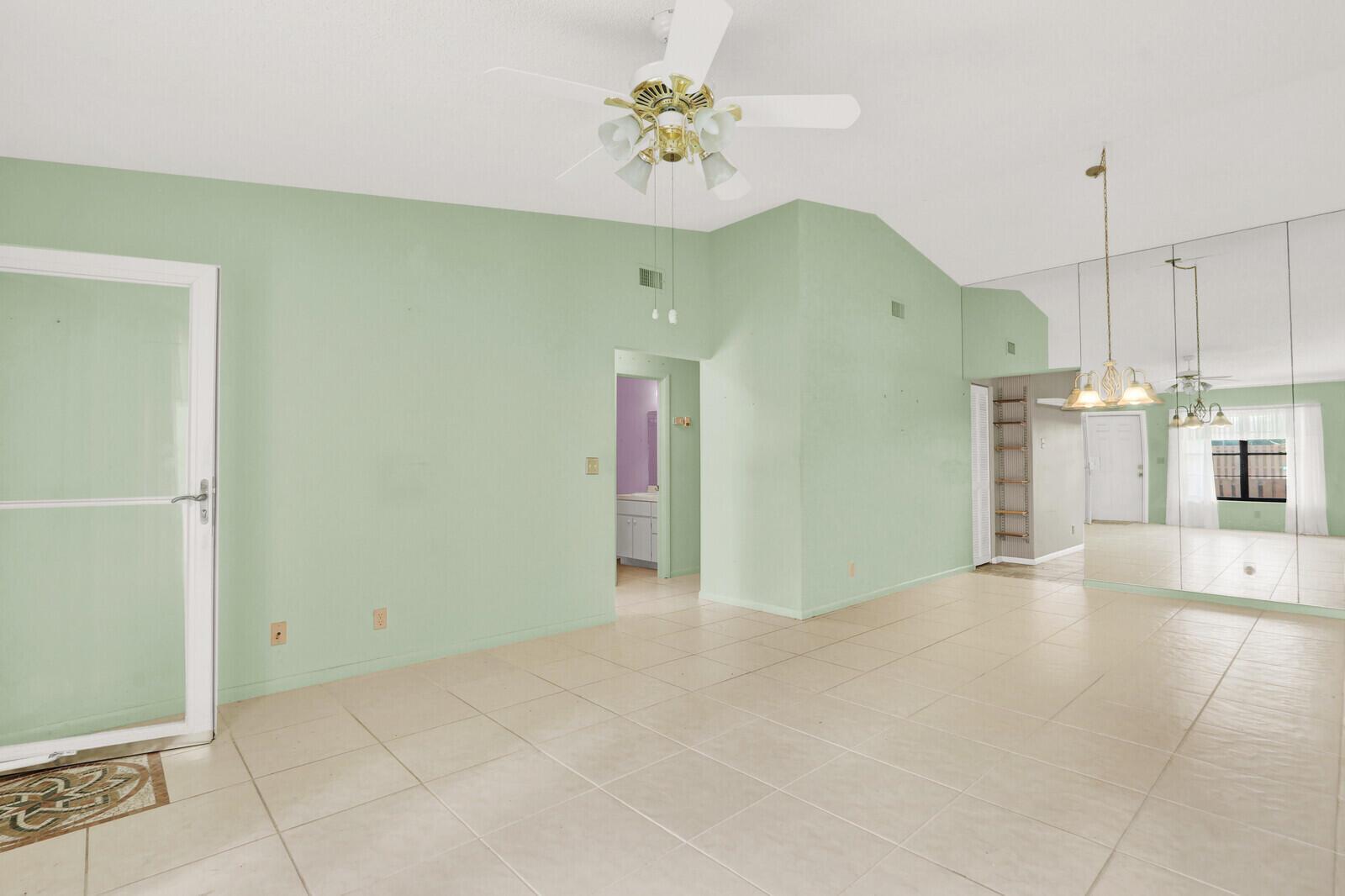 A room with light green walls, tiled floors, a ceiling fan, and a mirrored wall — 8091 SE Villa Circle, Hobe Sound FL 33455, HOBE SOUND, FL