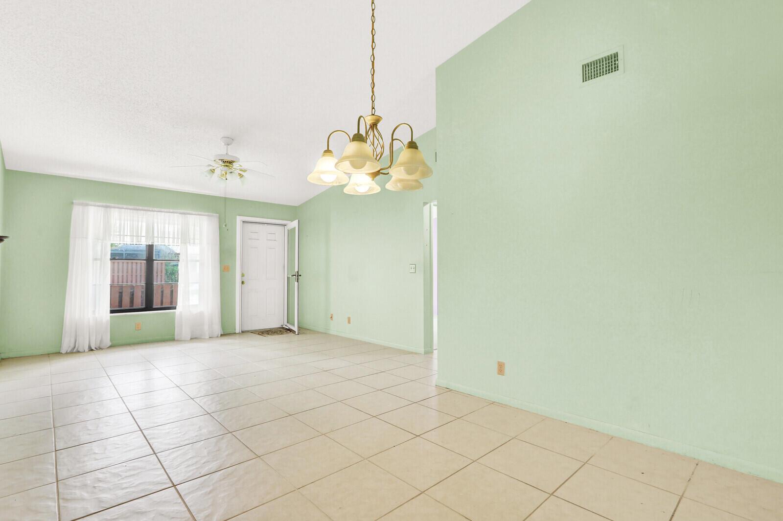 A living room with light green walls, tile flooring, a chandelier, and a front door — 8091 SE Villa Circle, Hobe Sound FL 33455, HOBE SOUND, FL