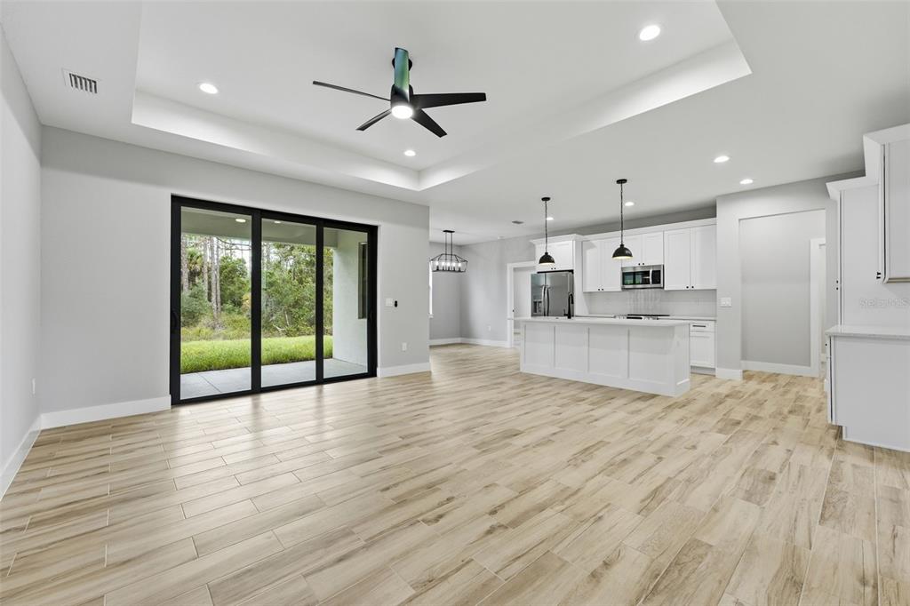 An open-concept kitchen and living area features wood-look tile flooring, white cabinetry, and sliding doors — 1113 SHERWIN STREET, PORT CHARLOTTE, FL