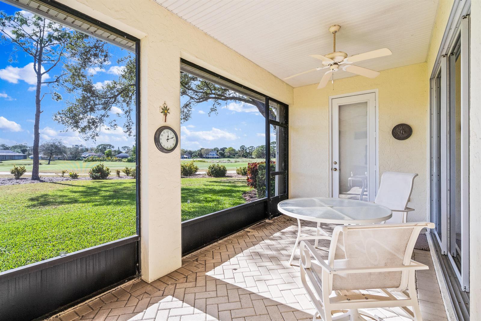 A screened-in patio features a glass table, white chairs, a ceiling fan, and golf course views — 747 Hampton Woods Lane SW, Vero Beach FL 32962, VERO BEACH, FL