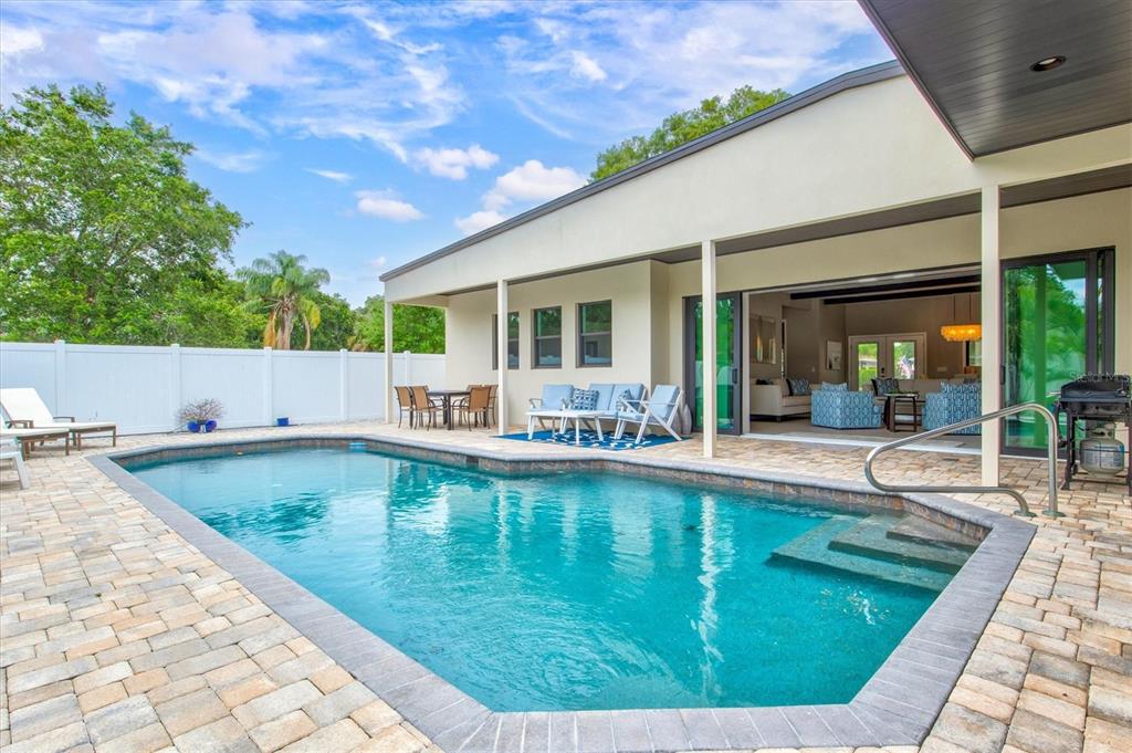 A swimming pool with a stone deck sits in front of a modern house exterior — 1905 TULIP DRIVE, SARASOTA, FL
