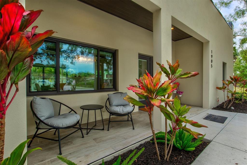 A modern covered porch features two chairs, a small table, and colorful tropical plants — 1905 TULIP DRIVE, SARASOTA, FL