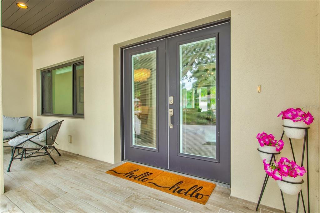 A covered patio features a double glass door, a welcome mat, and a tiered flower stand — 1905 TULIP DRIVE, SARASOTA, FL