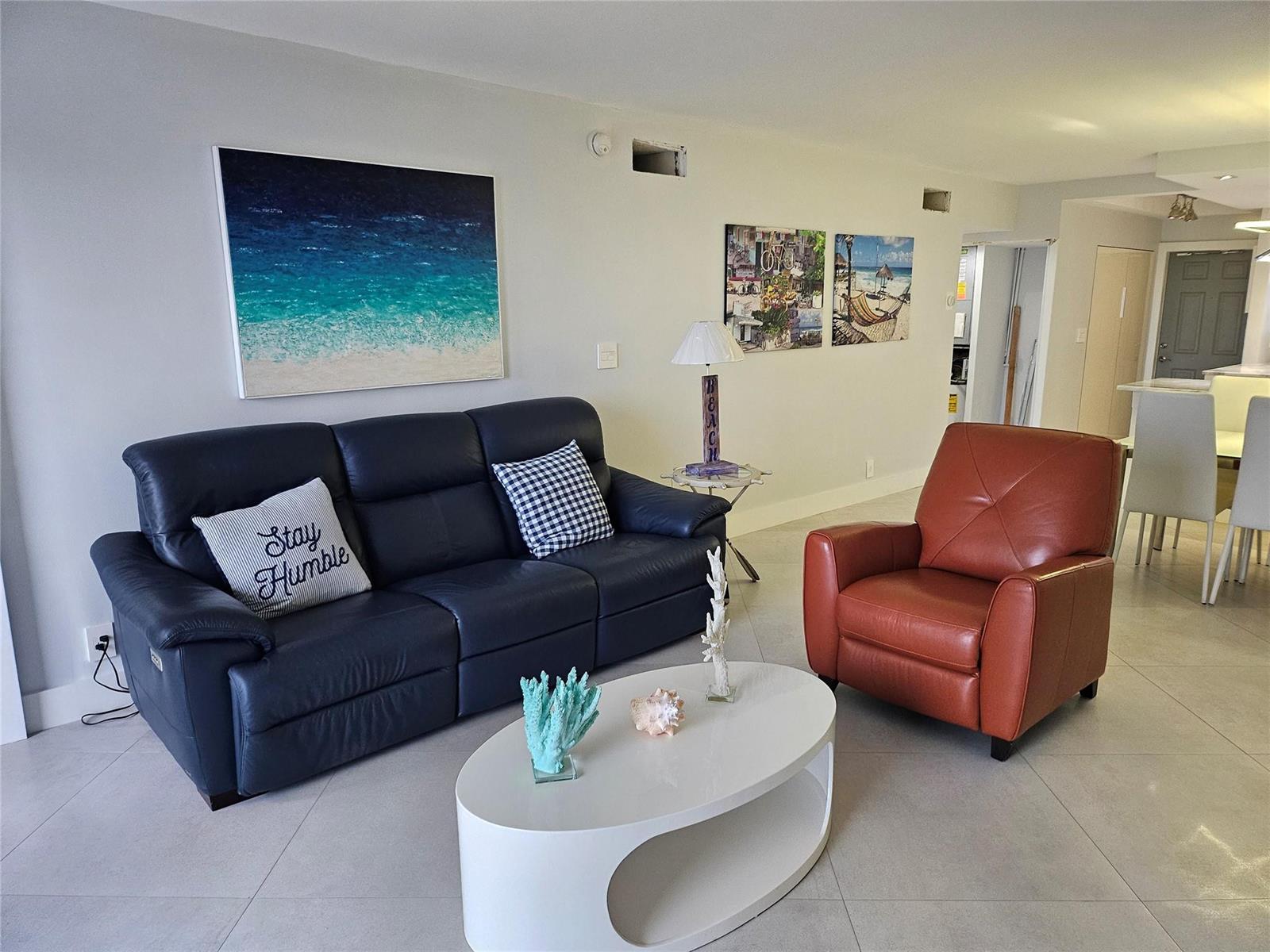 A living room features a navy sofa, a brown leather armchair, and a white coffee table — 750 N Ocean Boulevard # 503, Pompano Beach FL 33062, POMPANO BEACH, FL