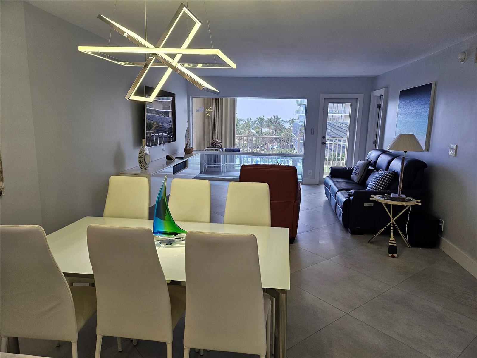 A dining area and living room with tile floors, a modern chandelier, and balcony access — 750 N Ocean Boulevard # 503, Pompano Beach FL 33062, POMPANO BEACH, FL