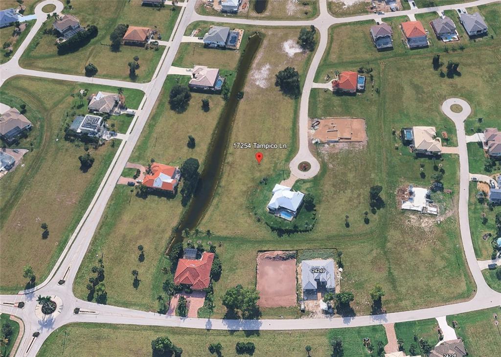 This aerial view shows a residential neighborhood with houses, a canal, and vacant lots — 17254 TAMPICO LANE, PUNTA GORDA, FL
