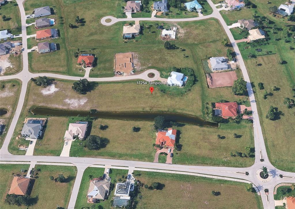 An aerial view shows a vacant residential lot situated between several houses and a pond — 17254 TAMPICO LANE, PUNTA GORDA, FL