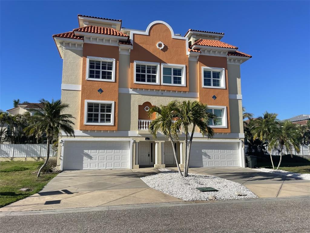 A three-story Mediterranean-style building features two garages, a central entrance, and palm trees — 136 175TH AVENUE E, REDINGTON SHORES, FL