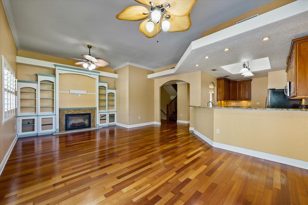 A living room with hardwood floors, a fireplace, built-in shelving, and an open kitchen — 136 175TH AVENUE E, REDINGTON SHORES, FL