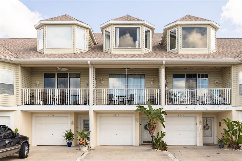 A three-unit townhouse exterior features beige siding, white garage doors, and second-story balconies — 8246 AQUILA STREET, PORT RICHEY, FL