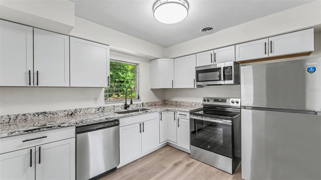 A kitchen features white cabinets, granite countertops, stainless steel appliances, and light wood-look flooring — 1725 31ST STREET NW, WINTER HAVEN, FL