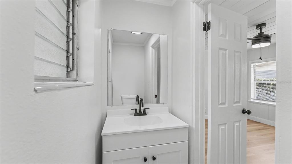 A small bathroom features a white vanity, a mirror, and an open door to another room — 1725 31ST STREET NW, WINTER HAVEN, FL