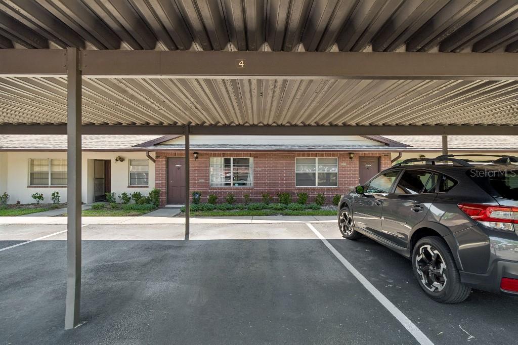 A covered parking space sits in front of a single-story brick apartment building — 2446 ENTERPRISE ROAD UNIT 4, CLEARWATER, FL