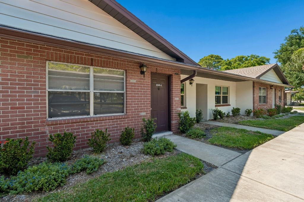 A single-story brick and stucco apartment building with a brown door and concrete walkway — 2446 ENTERPRISE ROAD UNIT 4, CLEARWATER, FL