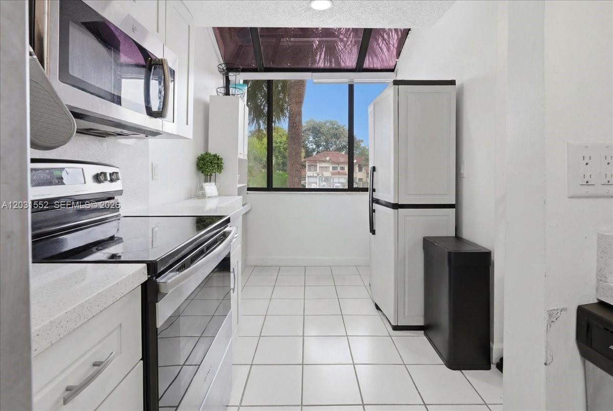 A galley kitchen features white cabinets, stainless steel appliances, tile flooring, and a large window — 9839 SW 138th Ave, Miami FL 33186, MIAMI, FL