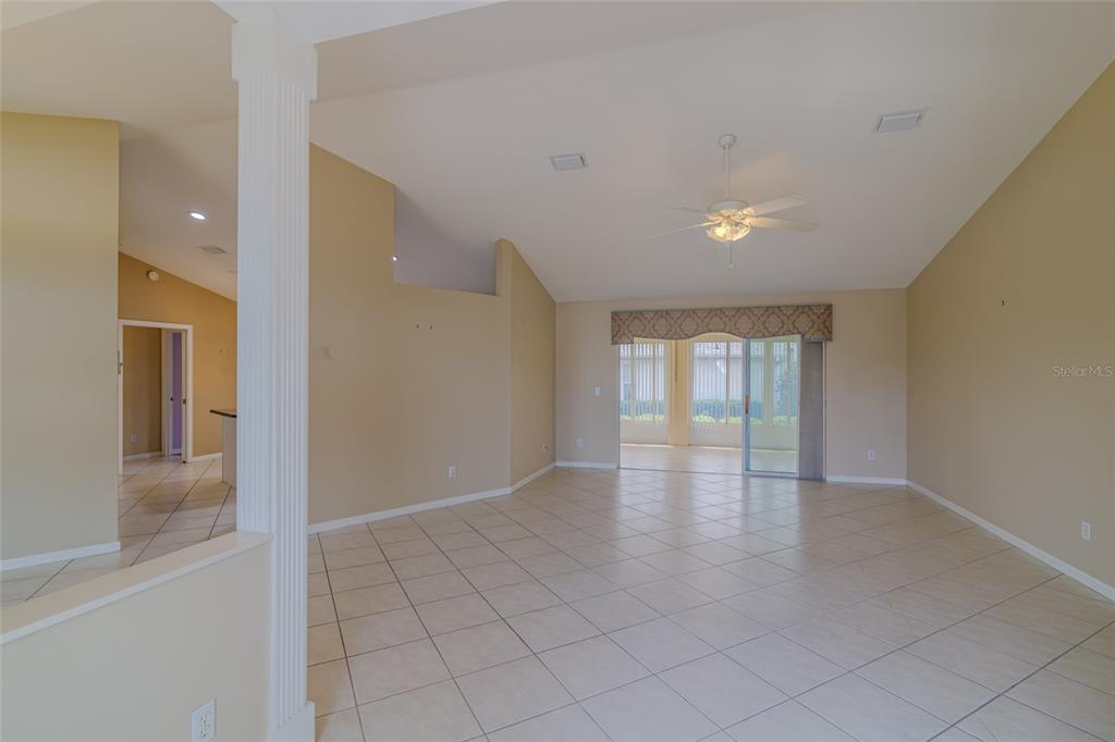 An open-concept living area features beige walls, tiled floors, a vaulted ceiling, and sliding doors — 2020 NW 50TH CIRCLE, OCALA, FL