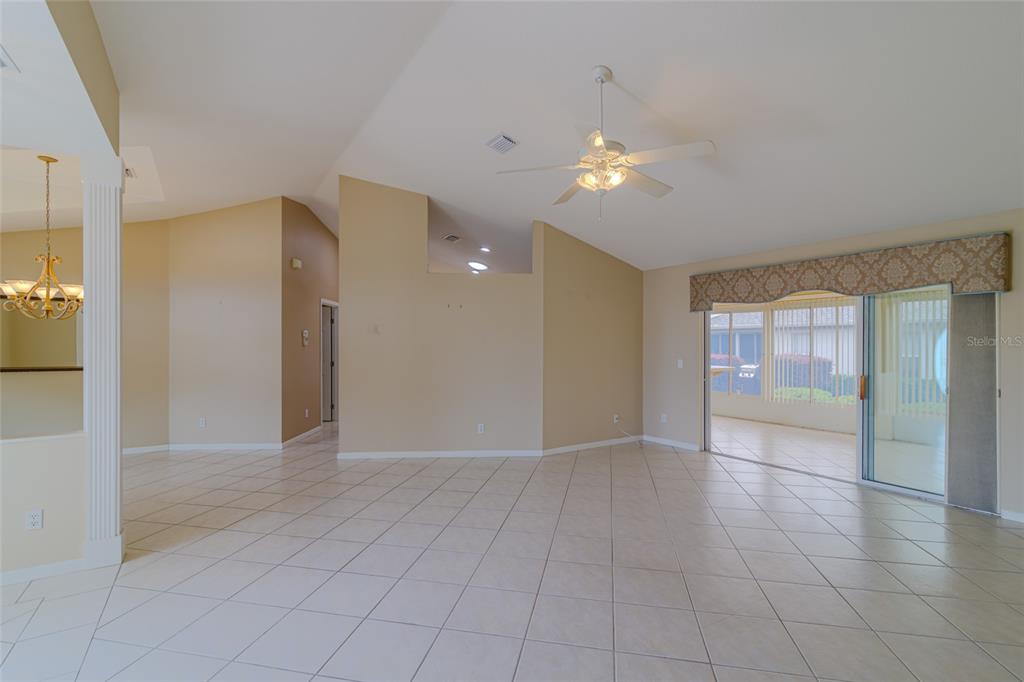 A spacious living area features beige tile flooring, vaulted ceilings, and a sliding glass door — 2020 NW 50TH CIRCLE, OCALA, FL