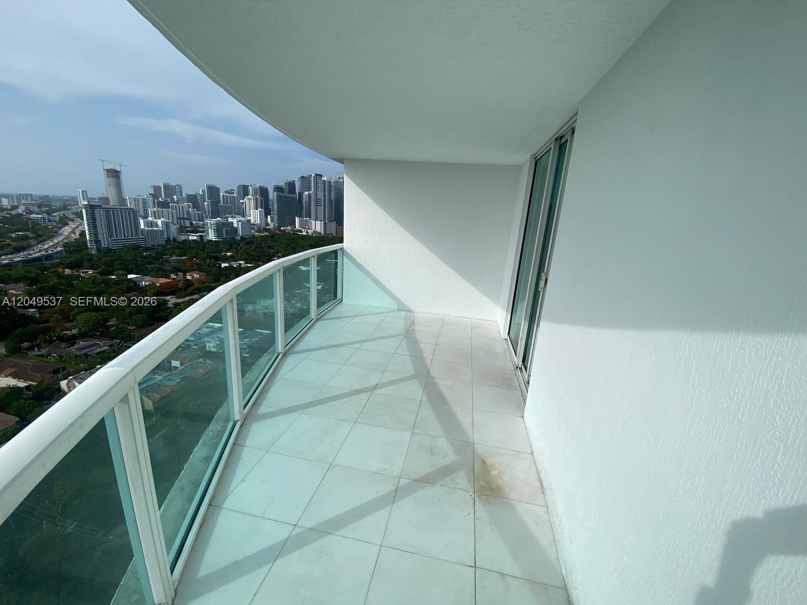 A high-rise balcony features white tile flooring, a glass railing, and a view of the city — 2101 Brickell Ave # 1112, Miami FL 33129, MIAMI, FL