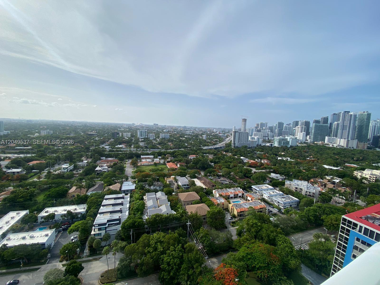An elevated view of a suburban neighborhood with dense trees and distant city skyscrapers — 2101 Brickell Ave # 1112, Miami FL 33129, MIAMI, FL