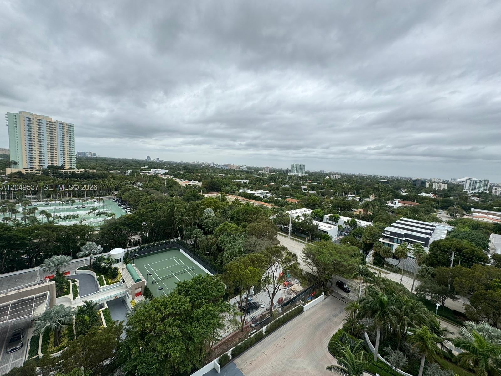 An elevated view shows a tennis court, lush trees, and surrounding buildings under a cloudy sky — 2101 Brickell Ave # 1112, Miami FL 33129, MIAMI, FL